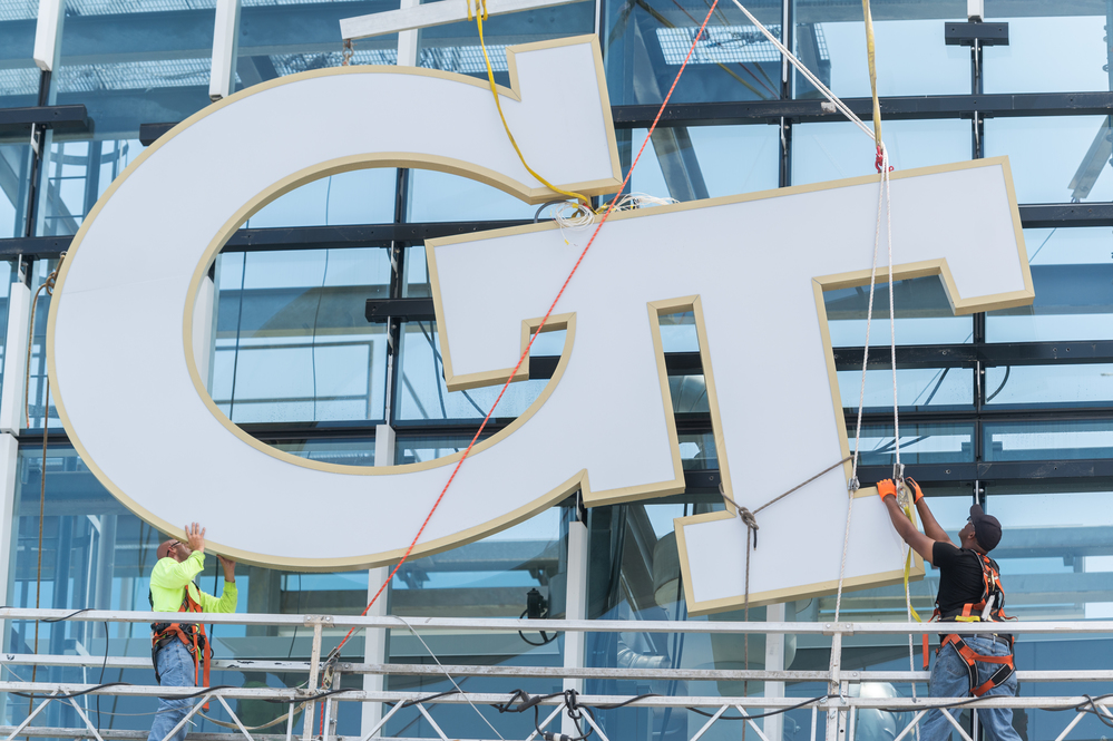 Construction featuring two men moving a huge Georgia Tech logo into place on a building